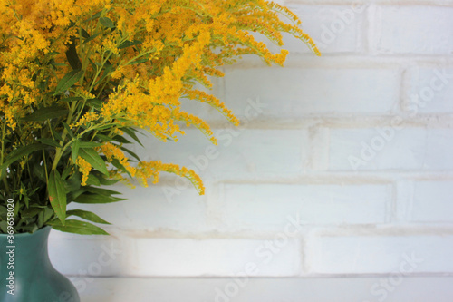 Bouquet of yellow flowers in vase on the white brick wall background. Autumn still life