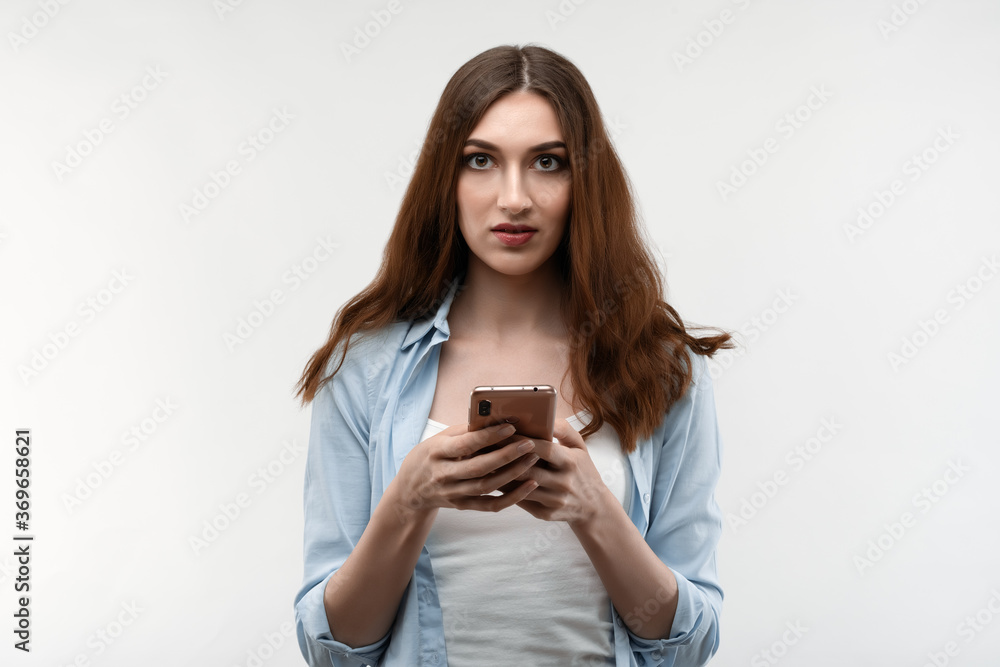 Young woman with long chestnut hair, dressed in casual clothes, using smartphone on white background Young woman with long chestnut hair, dressed in casual clothes, using smartphone on white background