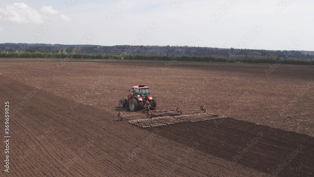 Aerial top view of tractor cutting furrows in farm field for sowing farm tractor with rotary harrow plow preparing land for sowing. Cultivator plows the land, working in a field. Aerial top view of tractor cutting furrows in farm field for sowing farm tractor with rotary harrow plow preparing land for sowing. Cultivator plows the land, working in a field.