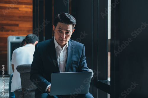 Serious businessman dressed in blue suit sitting in cafeteria and using laptop stock photo