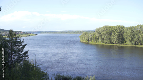 High Above River Looking Straight Down Through Thick Forest of Tall Evergreen Trees. Landscape with beautiful and relaxing river and forest trees on sunny summer day. Nature composition