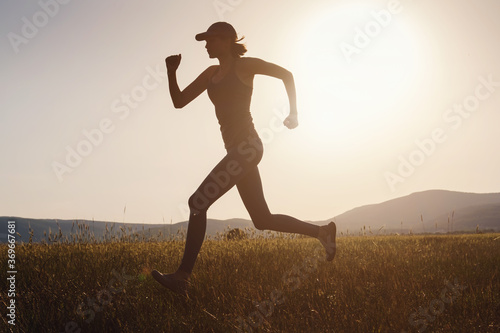 Jogging woman running in summer field at sunset