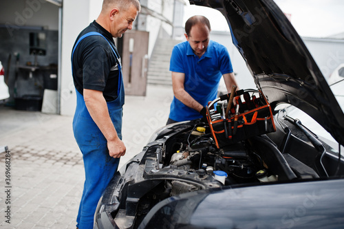 Car repair and maintenance theme. Two mechanics in uniform working in auto service, checking engine.