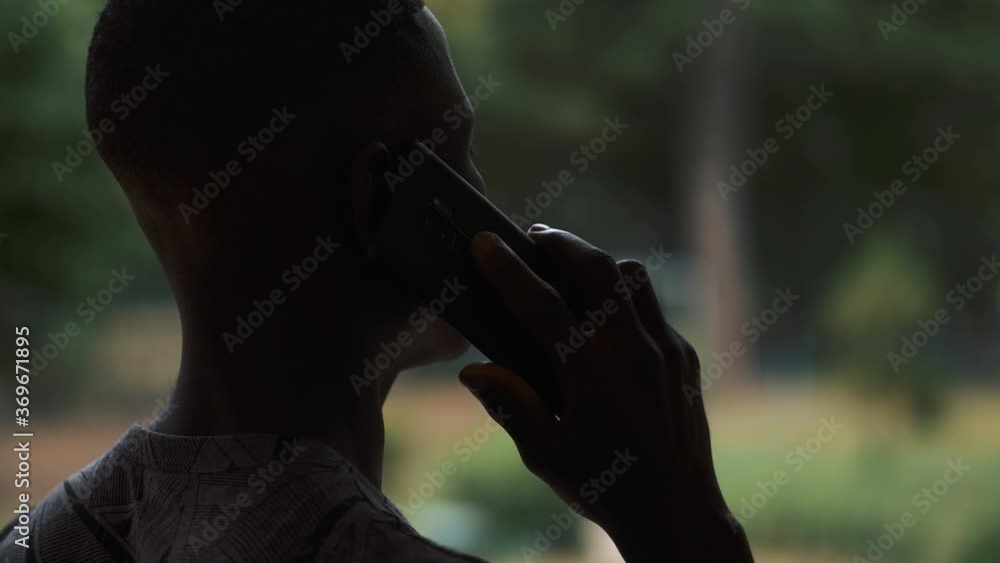 back view of young black man in dim light answering the phone back view of young black man in dim light answering the phone
