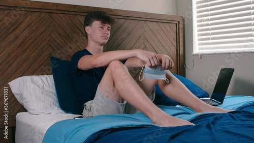 Sad teenage male distance learning at home on bed