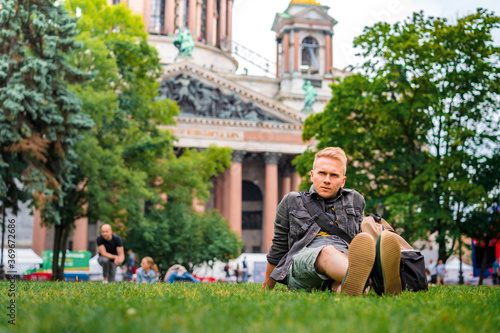 A young male tourist with a backpack visits the main sights of St. Petersburg, lying on the grass in front of St. Isaac's Cathedral photo