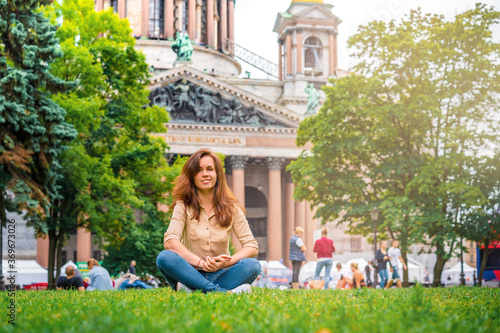 A female tourist is traveling in St. Petersburg, sitting on the grass in front of St. Isaac's Cathedral the main attraction of the city © KseniaJoyg