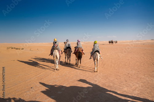 three people in Berber national robes on camel guided camels