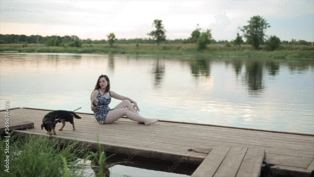 Joyful teenage girl plays with her des dog dachshund breed sitting on a wooden pier by the river on a summer day Joyful teenage girl plays with her des dog dachshund breed sitting on a wooden pier by the river on a summer day