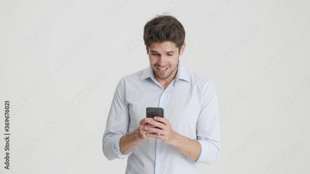 A happy man is doing winner gesture standing isolated and using his smartphone over white background A happy man is doing winner gesture standing isolated and using his smartphone over white background