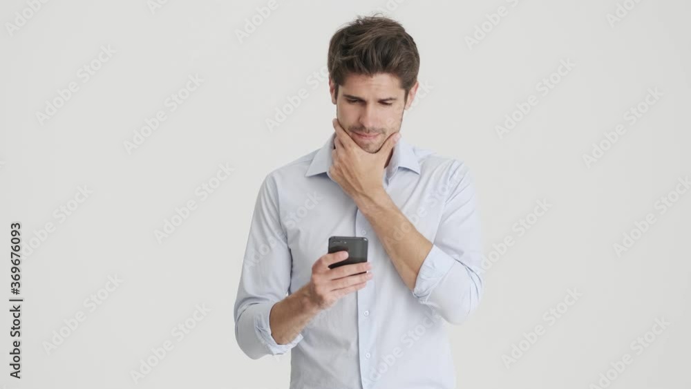A serious man is using his smartphone standing isolated over white background A serious man is using his smartphone standing isolated over white background