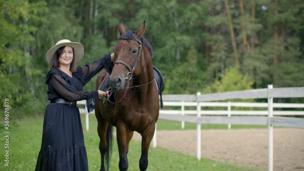 Beautiful woman in hat with brown horse on farm ranch. Attractive woman posing with purebred stallion on horse ranch. Scared woman with horse mare on summer pasture Beautiful woman in hat with brown horse on farm ranch. Attractive woman posing with purebred stallion on horse ranch. Scared woman with horse mare on summer pasture