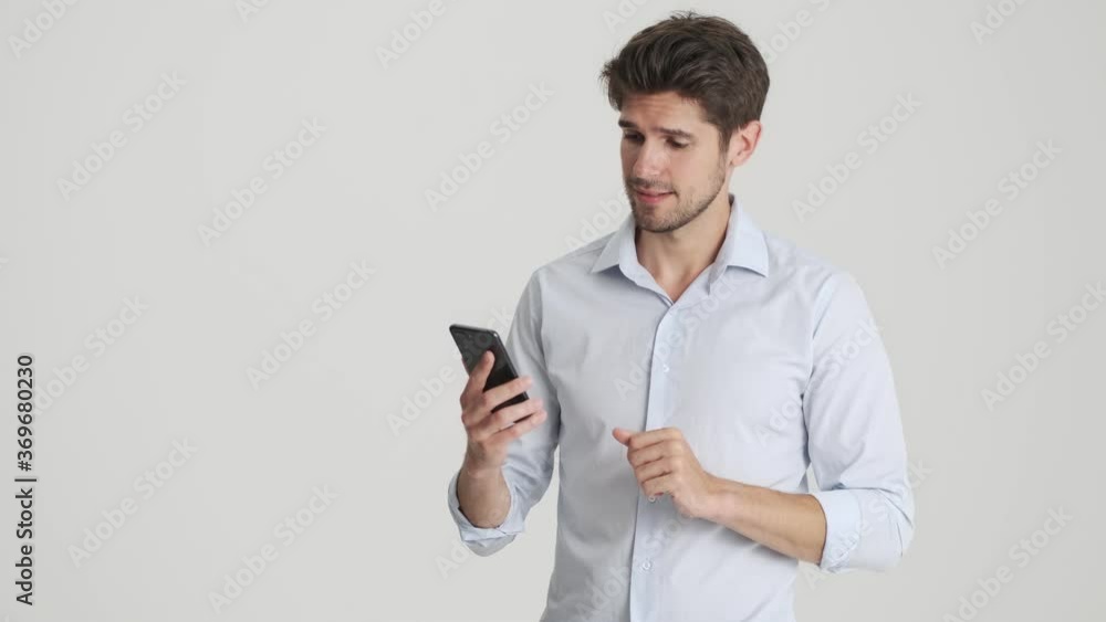 A focused man is typing on his smartphone standing isolated over white background A focused man is typing on his smartphone standing isolated over white background