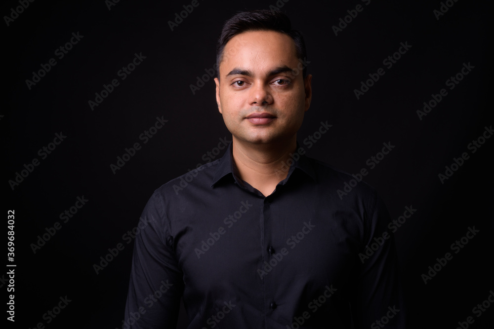 Fototapeta premium Portrait of young handsome Indian businessman against black background