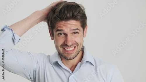 A close-up view of a puzzled young man is shrugging his shoulders standing isolated over white background