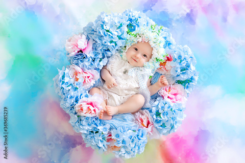 beautiful baby 6 months in a hat made of flowers, lying in a basket with hydrangeas on a blue background, a small child among flowers