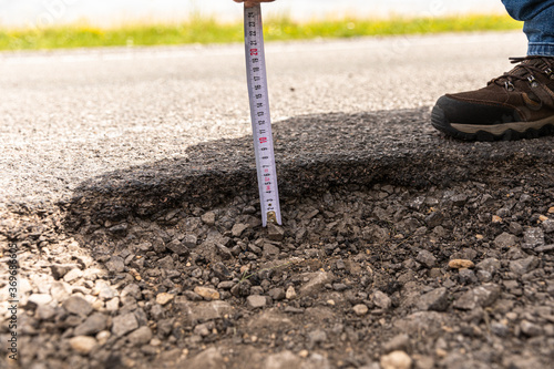 Closeup of a person measuring the thickness of asphalt with a tape under the sunlight