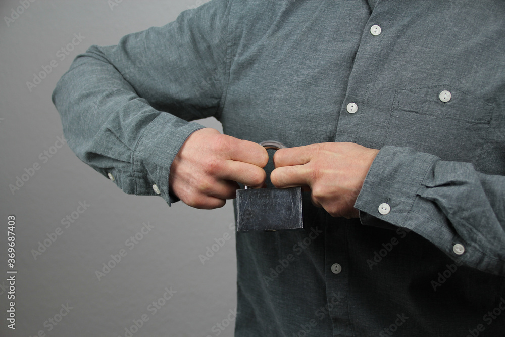 man in a gray shirt holds a closed iron lock in his hands, trying to break it, concept of difficulties, close-up