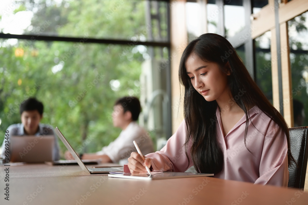 A secretary woman is writing on a computer tablet while sitting in the meeting room. A secretary woman is writing on a computer tablet while sitting in the meeting room.