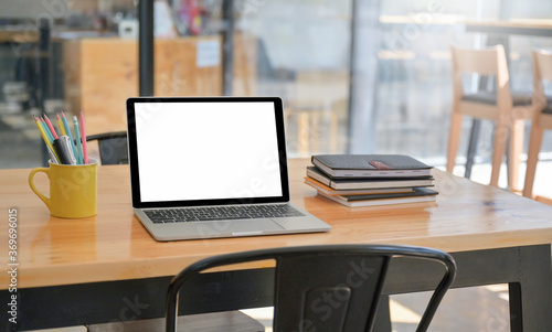 A laptop and notebook with stationery are placed on the table in the comfortable workspace.