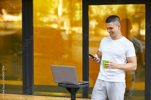 Portrait of a young man standing in the street with a laptop.