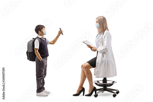 Schoolboy in a uniform with a face mask showing a smartphone to a female doctor