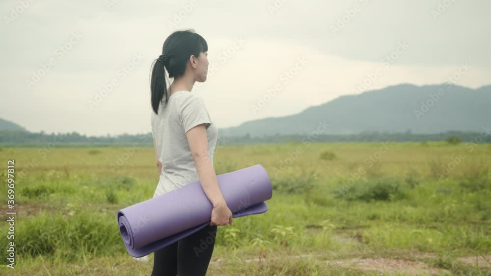 Attractive asian woman standing and holding yoga mat in the beautiful mountains view during the morning. health and wellness concept. Attractive asian woman standing and holding yoga mat in the beautiful mountains view during the morning. health and wellness concept.