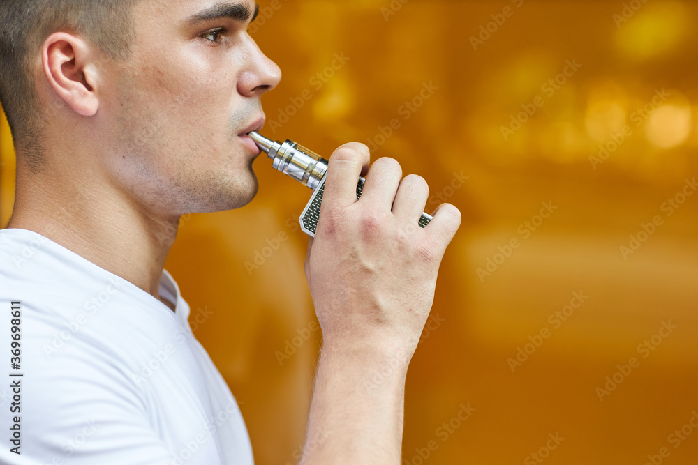A young man standing on the street smokes a vape and blows smoke. A young man standing on the street smokes a vape and blows smoke.