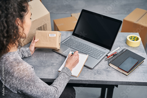 Woman sending parcel using her laptop and notepad. Working from home