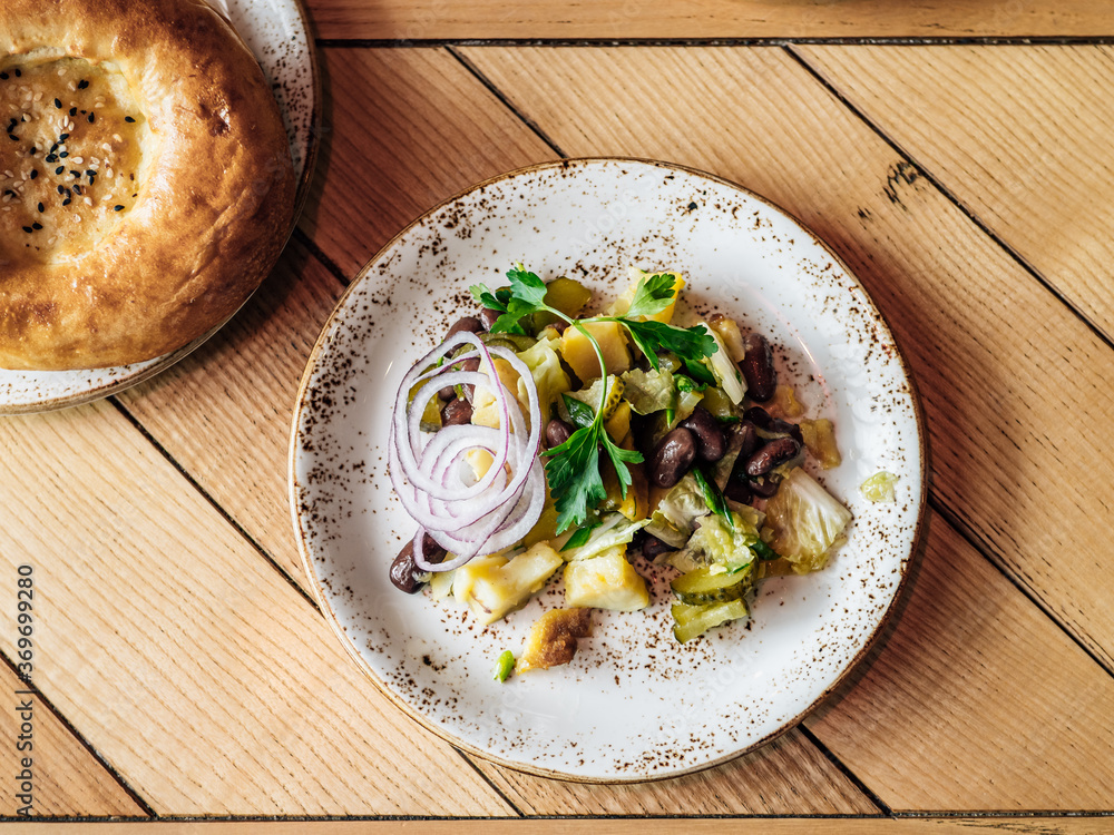 Authentic shot of georgian style salad with red beans, potatoes, salted cucumber on rustic wooden tabletop.