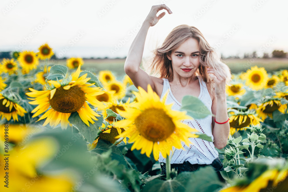 Young, slender girl in a white T-shirt poses at sunset in a field of sunflowers Young, slender girl in a white T-shirt poses at sunset in a field of sunflowers