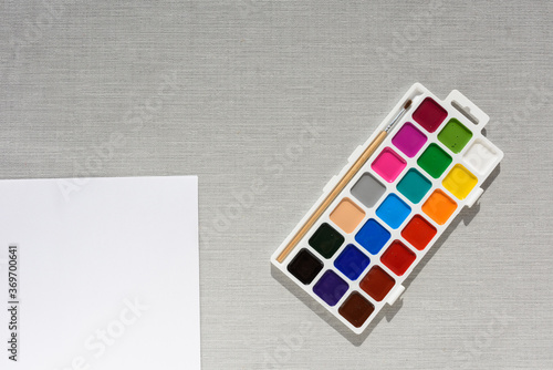 Brush, pallet watercolor paint and empty sheet of paper on grey background. no people. Top view. copy space. Workplace artist. drawing kit. fine art, creativity, painting and artistic tools concept
