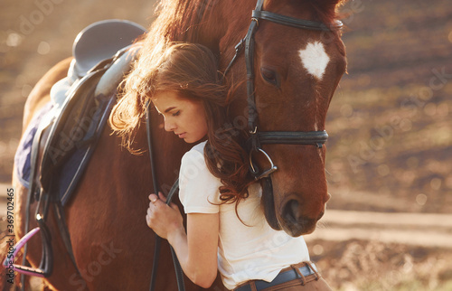 Young woman embracing her horse in agriculture field at sunny daytime