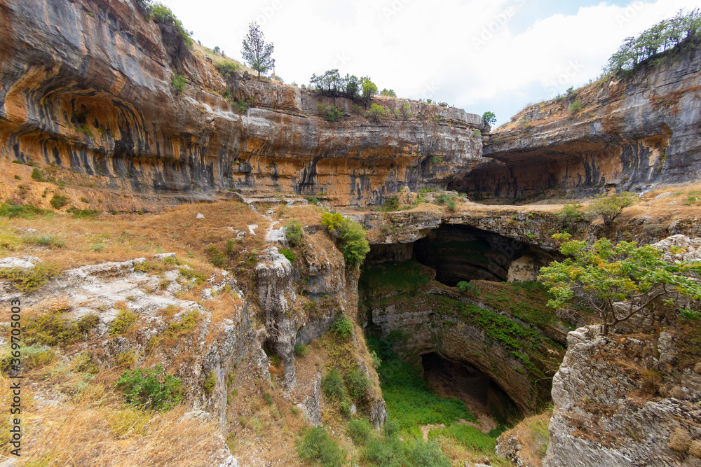 Baatara gorge waterfall in Lebanon. Balaa Sinkhole caves and formations covered with green plants and dry grass. Natural stone bridges