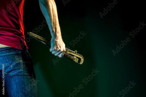 A male construction worker holds spanner in his hand on a dark background