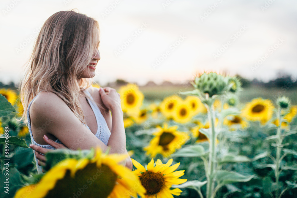 Young, slender girl in a white T-shirt poses at sunset in a field of sunflowers Young, slender girl in a white T-shirt poses at sunset in a field of sunflowers