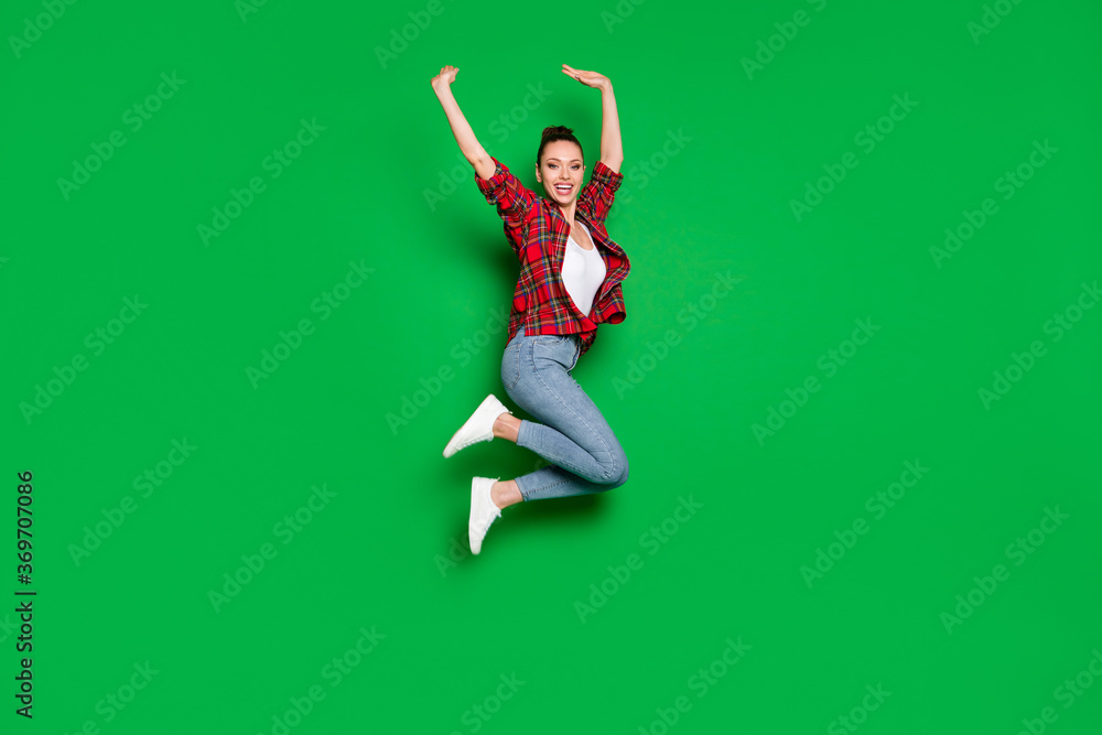 Full length body size view of her she nice attractive glad cheerful cheery girl in checked shirt jumping rising hands up having fun isolated on bright vivid shine vibrant green color background Full length body size view of her she nice attractive glad cheerful cheery girl in checked shirt jumping rising hands up having fun isolated on bright vivid shine vibrant green color background