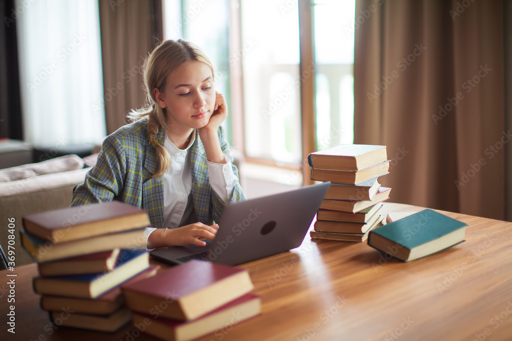 Young cute teen schoolgirl student sitting with books and working at laptop. Back to school. Exam preparation Young cute teen schoolgirl student sitting with books and working at laptop. Back to school. Exam preparation