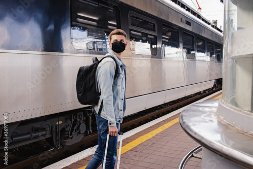 Young man wearing protective face mask standing on the railway station near the train.