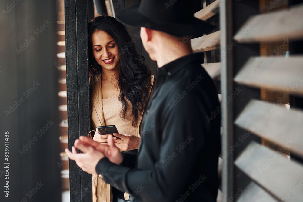 Woman with black curly hair and her man standing together near wooden windows Woman with black curly hair and her man standing together near wooden windows