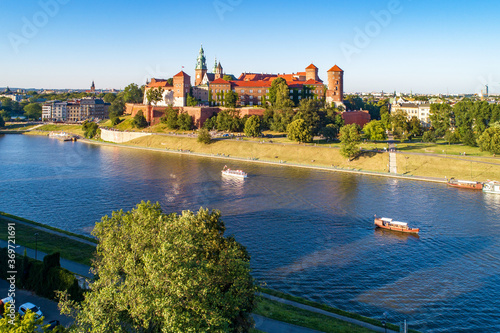Royal Wawel Cathedral and castle in Krakow, Poland. Aerial view in sunset light. Vistula River, tourist boats, riverbanks with parks, trees. promenade and walking people