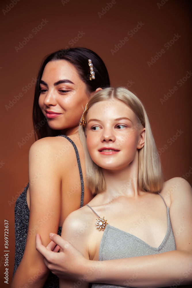 two pretty diverse girls happy posing together: blond and brunette on brown background, lifestyle people concept two pretty diverse girls happy posing together: blond and brunette on brown background, lifestyle people concept