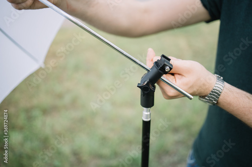 Close-up view of male hands placing umbrella diffuser to stand. Cropped man setting umbrella diffuser with tripod outdoor.