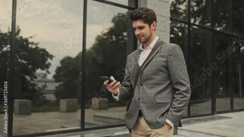 Wallpaper Mural Happy handsome businessman having call then talking by smartphone while walking near the building Torontodigital.ca