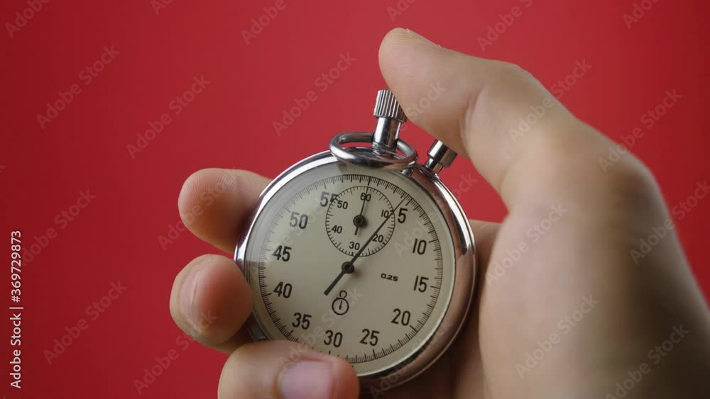 Male hand holding analogue stopwatch on red background. Time start with old chronometer man presses start button in the sport concept. Time management concept. Male hand holding analogue stopwatch on red background. Time start with old chronometer man presses start button in the sport concept. Time management concept.