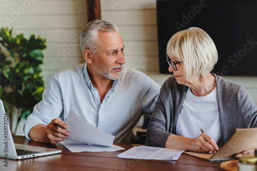 Aged couple signing and filling documents at home