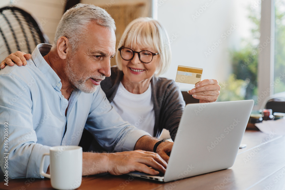 Happy senior couple using laptop and credit card for online shopping at home living room