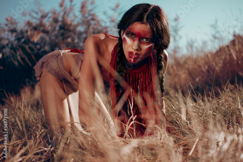 red-skinned Indian girl with red makeup on her face posing in yellow grass photo