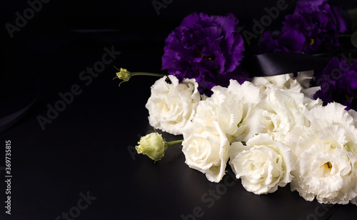 Funeral flowers of white and purple eustoma on a black background. Copy space
