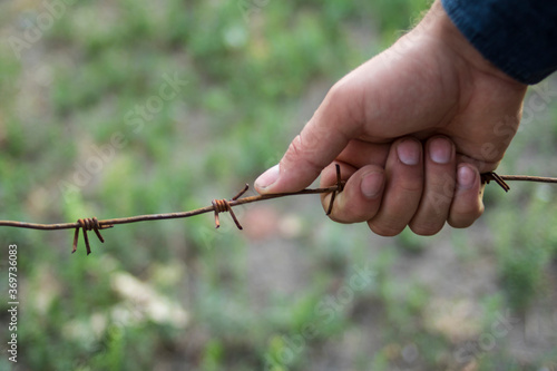 A guy holding an iron rusty barbed wire with his hand